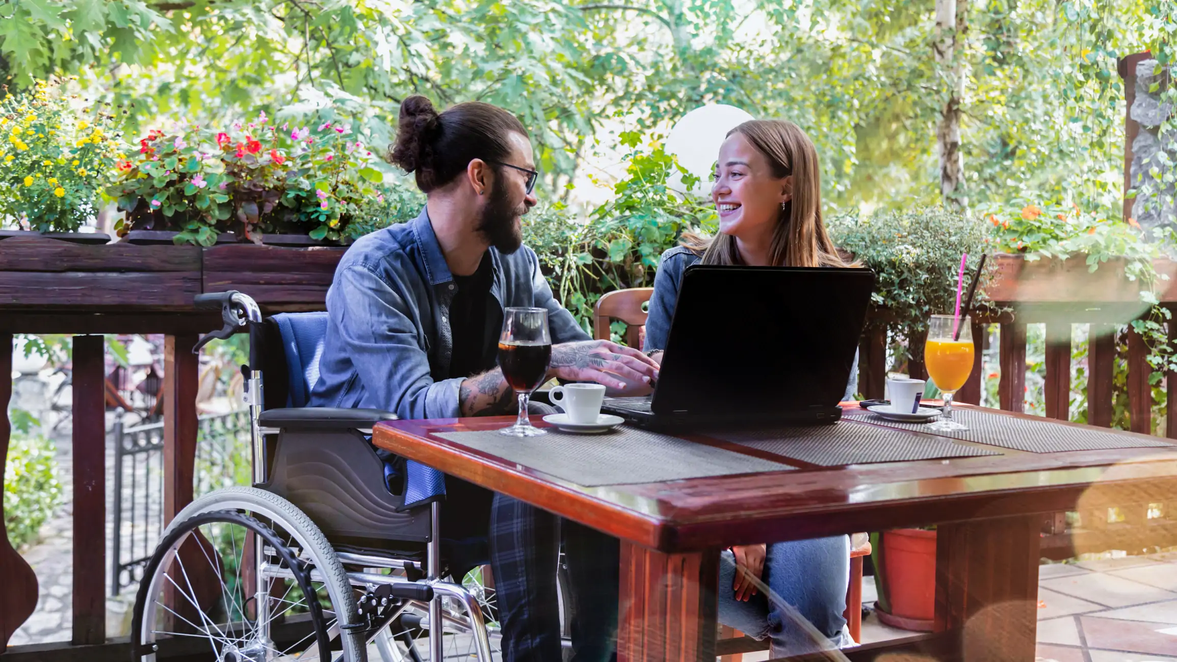 man in wheelchair is socialising with a friend in outdoor table in a restaurant